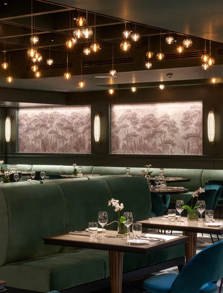 Sedute del ristorante Hilton Rome EUR La Lama con divani in velluto verde e tavoli dalle linee essenziali, lampade dorate creano un ambiente accogliente e sofisticato.