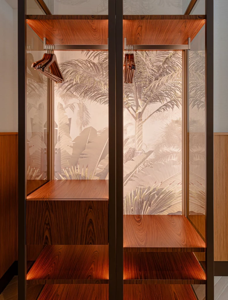 Armadio a vista con struttura in vetro e legno, fondo decorato con motivo tropicale tono su tono.