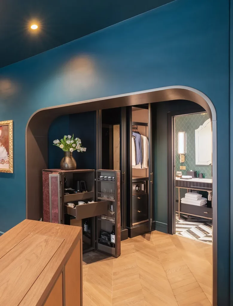 Dettaglio guardaroba integrato con minibar e accessori, pavimento in legno a spina e vista sul bagno