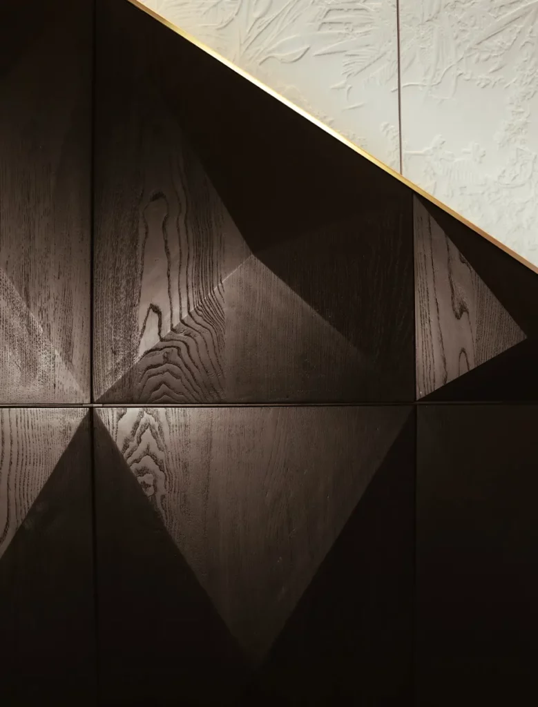 Dettaglio della parete con boiserie in legno scuro con lavorazione geometrica tridimensionale
