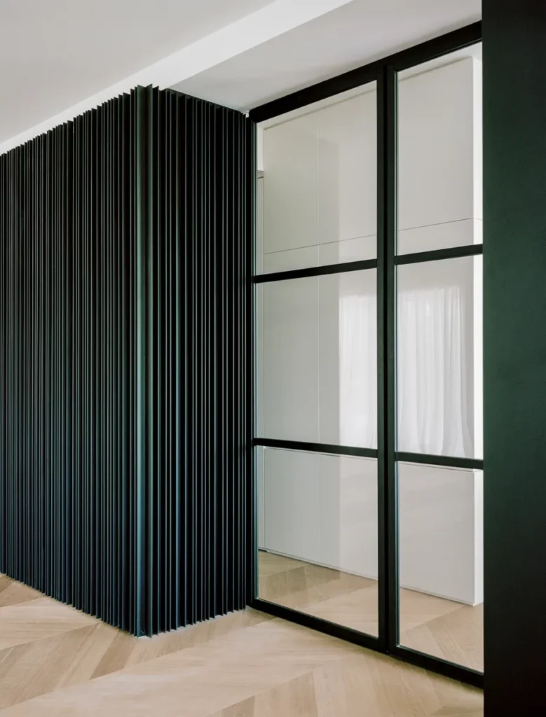 Parete attrezzata con pannelli verticali in legno scuro realizzati da Antonacci falegnameria, abbinata a porta scorrevole in vetro e metallo nero, con pavimento in legno a spina di pesce