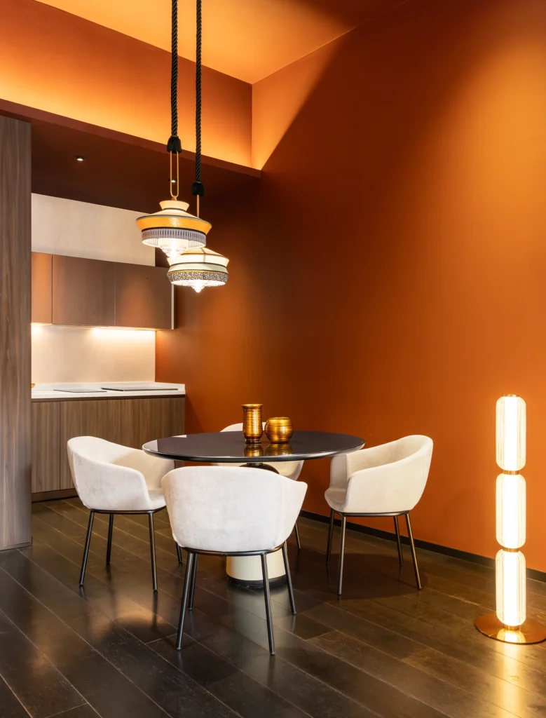 Zona pranzo di Palazzo Rota con pareti arancio, tavolo rotondo e sedute in velluto chiaro, arredi su misura di Antonacci Falegnamerie
